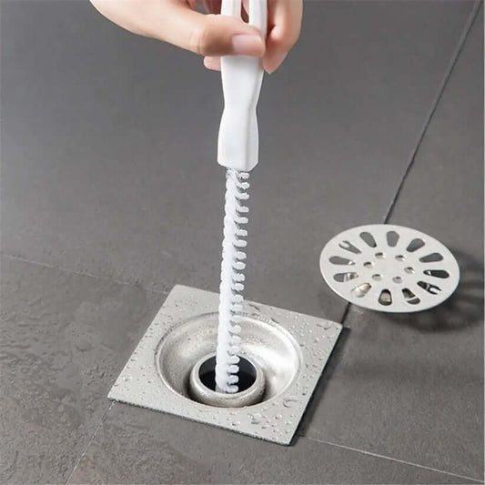 A person using a cleaning brush to remove debris from a kitchen sink drain.