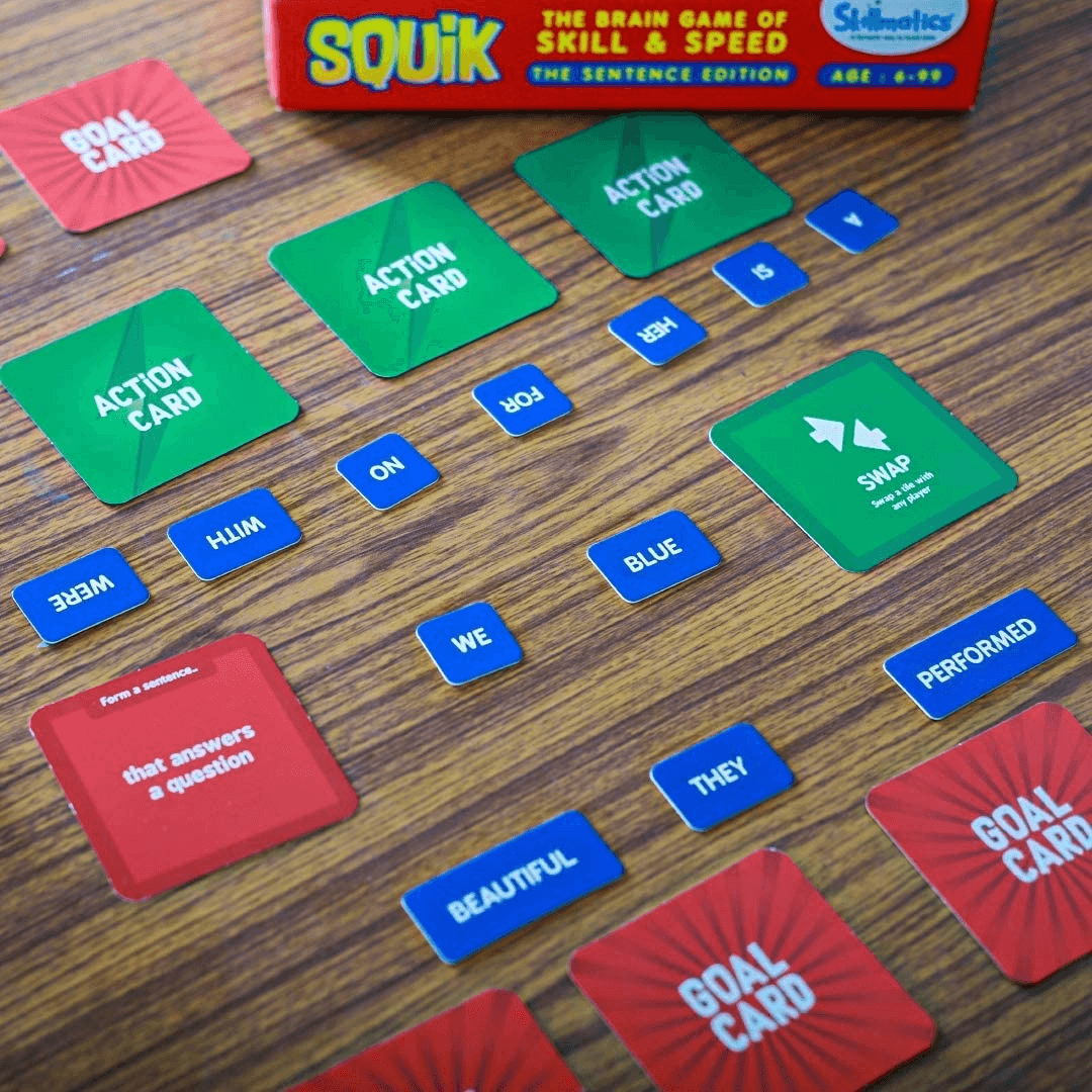 "SQUIK The Sentence Edition game with word tiles, goal, and action cards on a table, promoting educational fun for kids."