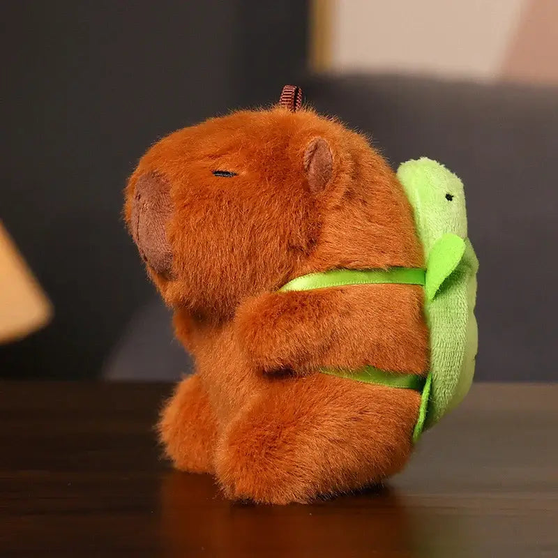 Cute brown Capibara plush keychain with turtle backpack, soft toy on a table.
