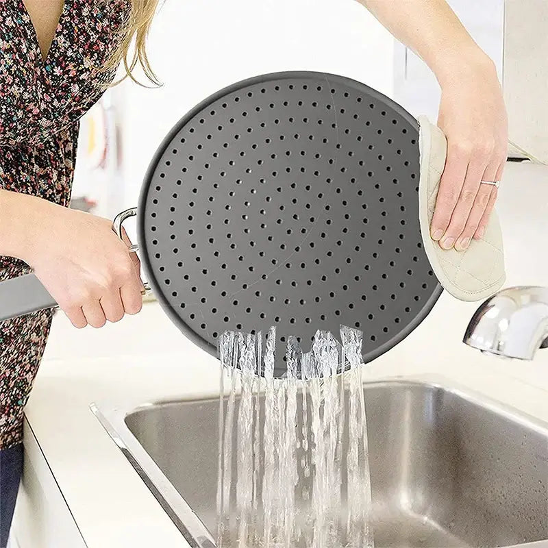 Person washing a silicone kitchen splatter screen with a handle over a sink, showing its oil splash guard and heat-resisting features.