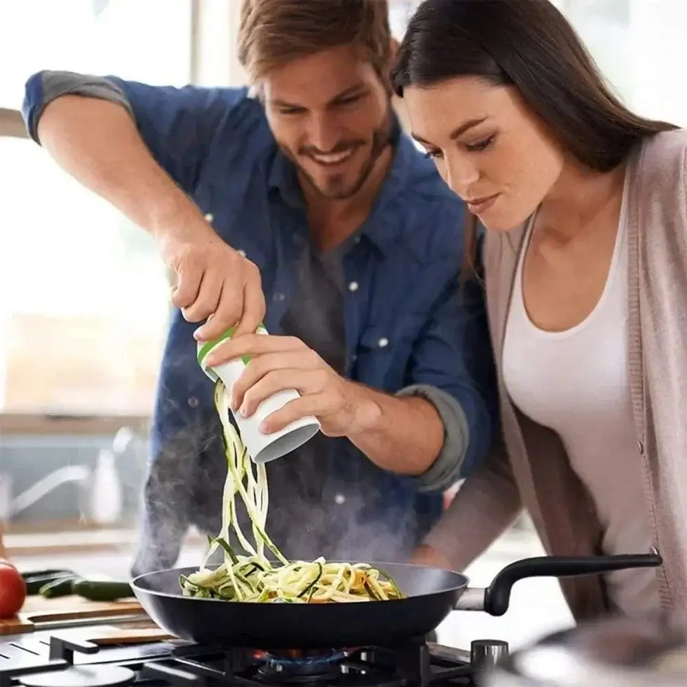 Couple using a spiralizer to prepare zucchini noodles in a frying pan, showcasing a fun cooking experience.