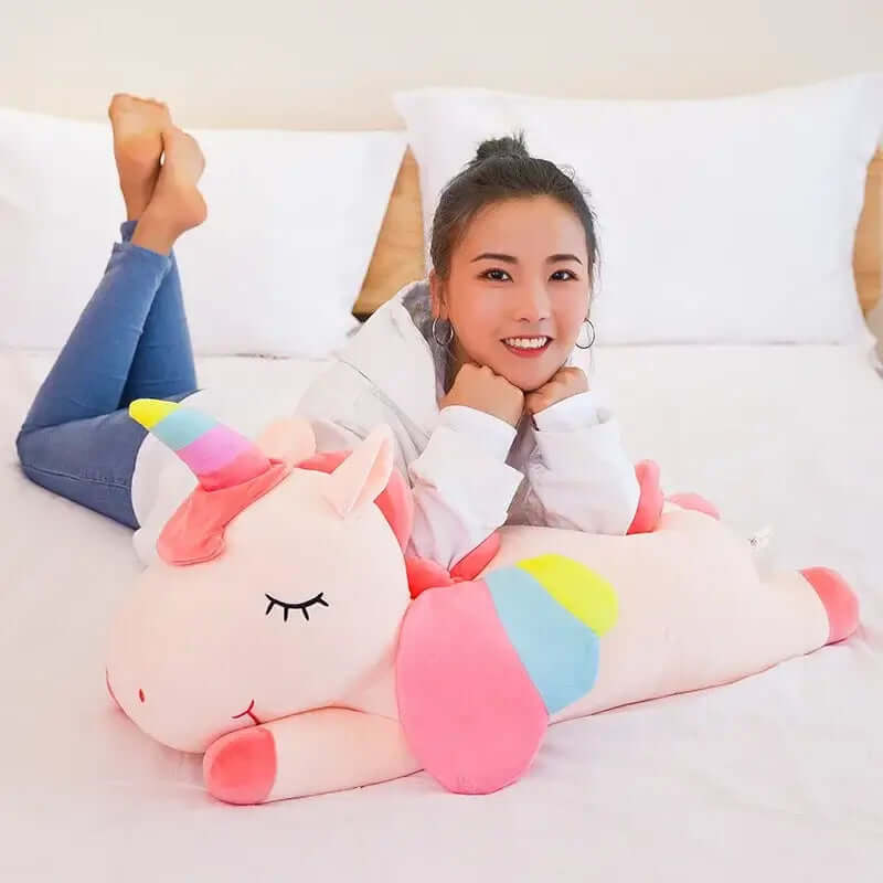 Smiling girl laying with a pastel Kawaii unicorn plush toy on a bed, showcasing its soft and cuddly design.