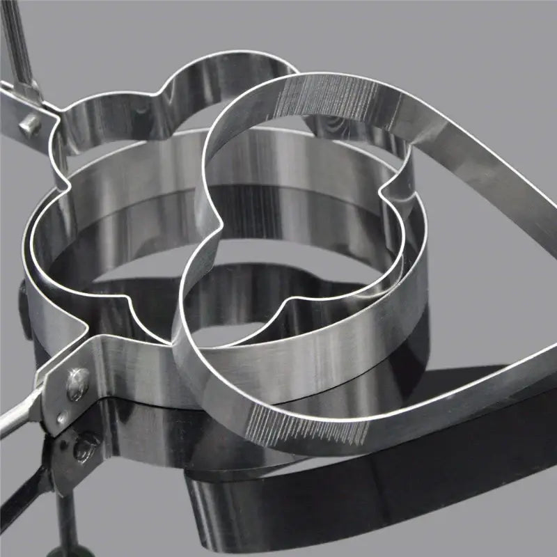 Stainless steel egg mold rings in heart and flower shapes for cooking pancakes and eggs in creative designs.