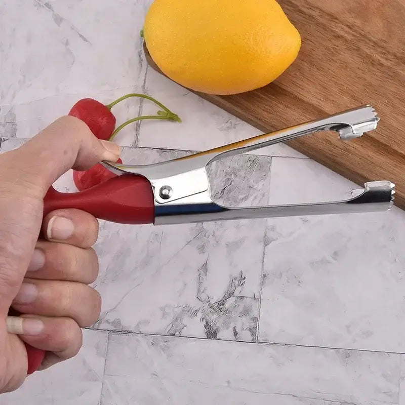 Hand holding a stainless steel apple corer tool with red handle near lemon and chili peppers on a kitchen counter.