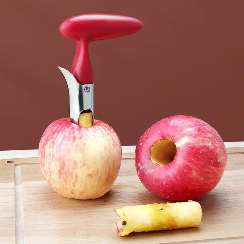 Stainless steel apple corer with red handle, removing seeds from a fresh apple on a wooden cutting board.